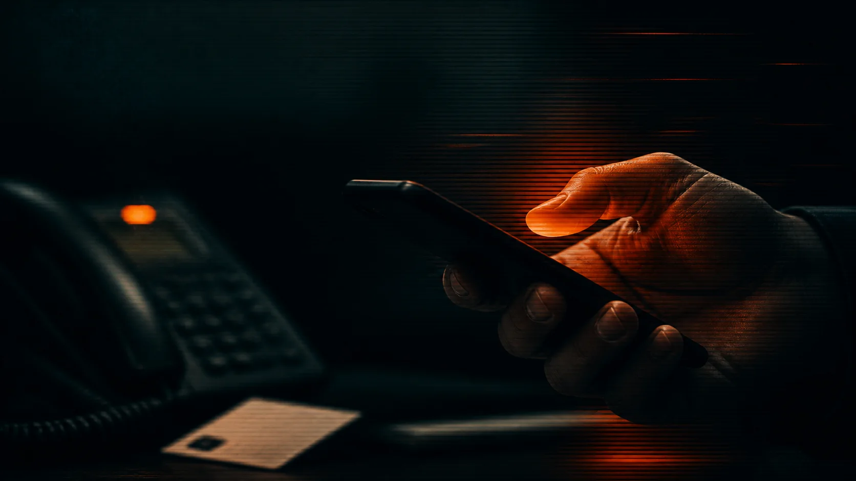 A hand using a mobile phone beside a desk phone